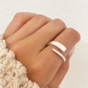 Könnte beinhalten: Ein silberner Ring mit einem einzigartigen, offenen Design. Der Ring besteht aus einem einzigen Stück Metall, das zu einer geschwungenen Form gebogen ist.