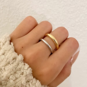 May include: Two simple gold and silver rings worn on a finger. The rings are both thin and have a rounded shape.