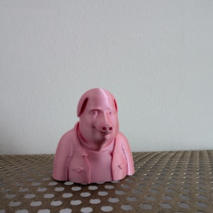 Puede incluir: Un busto de cerdo impreso en 3D de color rosa, que lleva una chaqueta. El cerdo tiene una cara detallada y la cabeza ligeramente inclinada.