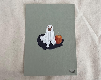 Puede incluir: Ilustración con temática de Halloween en una tarjeta gris. Presenta un perro disfrazado de fantasma, con una sábana blanca sobre él. Una pequeña calabaza naranja está al lado del perro. La obra está firmada en la esquina inferior derecha.