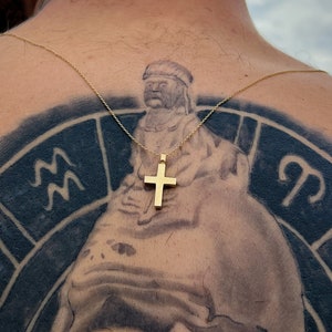 May include: A person with a black and white tattoo of a zodiac wheel on their back. The tattoo features a woman's face, astrological symbols, and a small gold cross pendant.