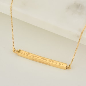 May include: Gold bar necklace with the inscription "Still need you close so I can breathe".