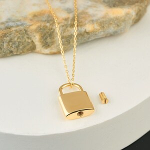May include: A gold chain necklace with a padlock pendant. The padlock has a small screw on the side.