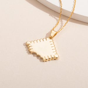 May include: A gold necklace with a pendant shaped like a bitten cookie. The pendant has a white enamel finish and a detailed scalloped edge.