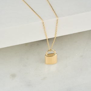May include: A gold chain necklace with a padlock pendant. The padlock is a simple, solid design.