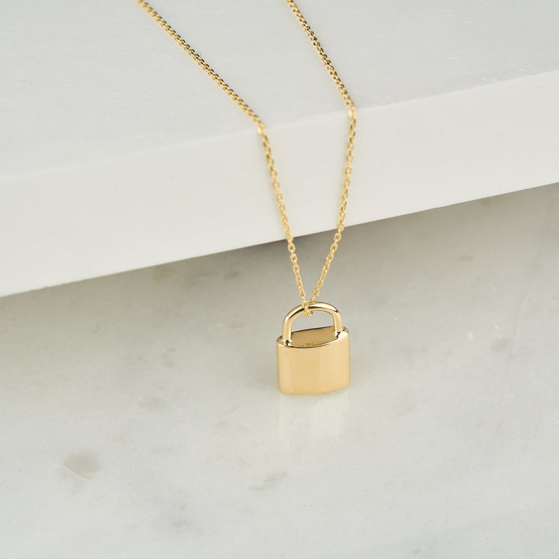 May include: A gold chain necklace with a padlock pendant. The padlock is a simple, solid design.