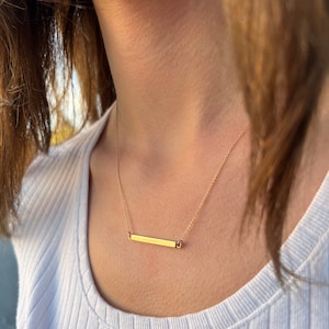 May include: A gold bar necklace with a delicate chain. The bar is simple and sleek, with a subtle shine.