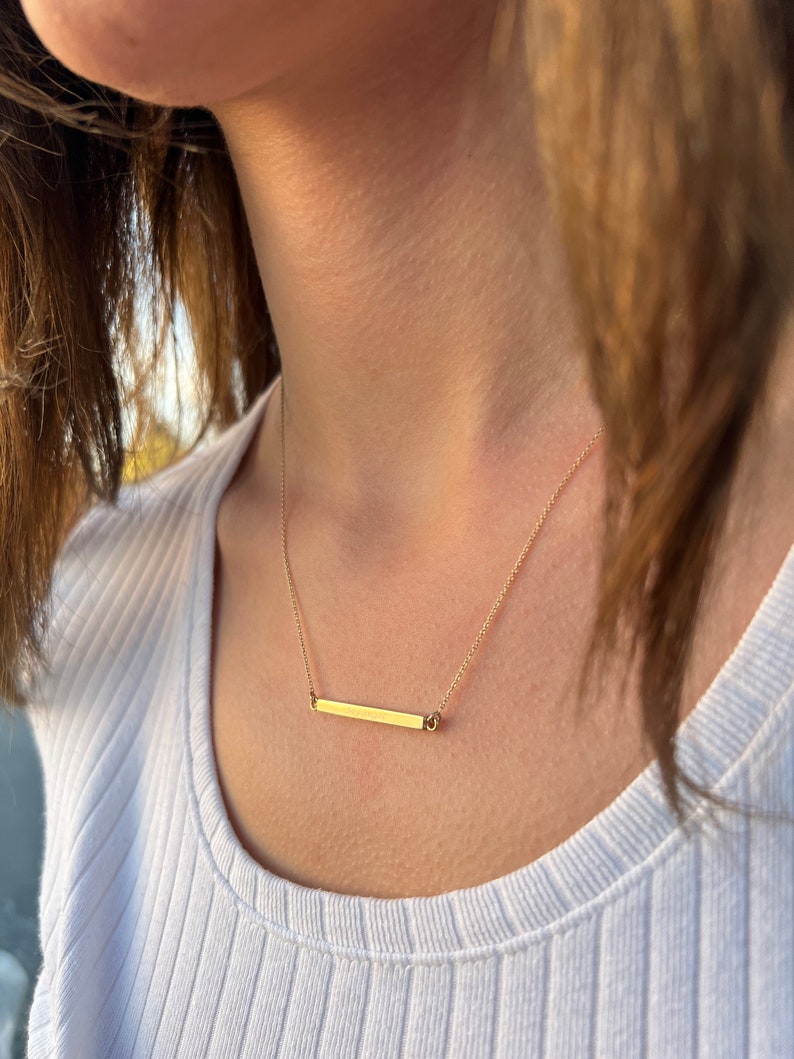 May include: A gold bar necklace with a delicate chain. The bar is simple and sleek, with a subtle shine.