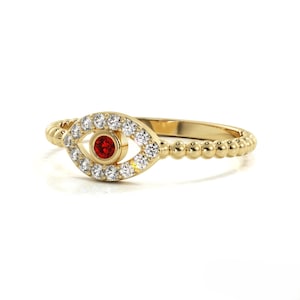 May include: A gold ring with a beaded band and an evil eye design. The eye is surrounded by small white stones and has a red gemstone in the center.