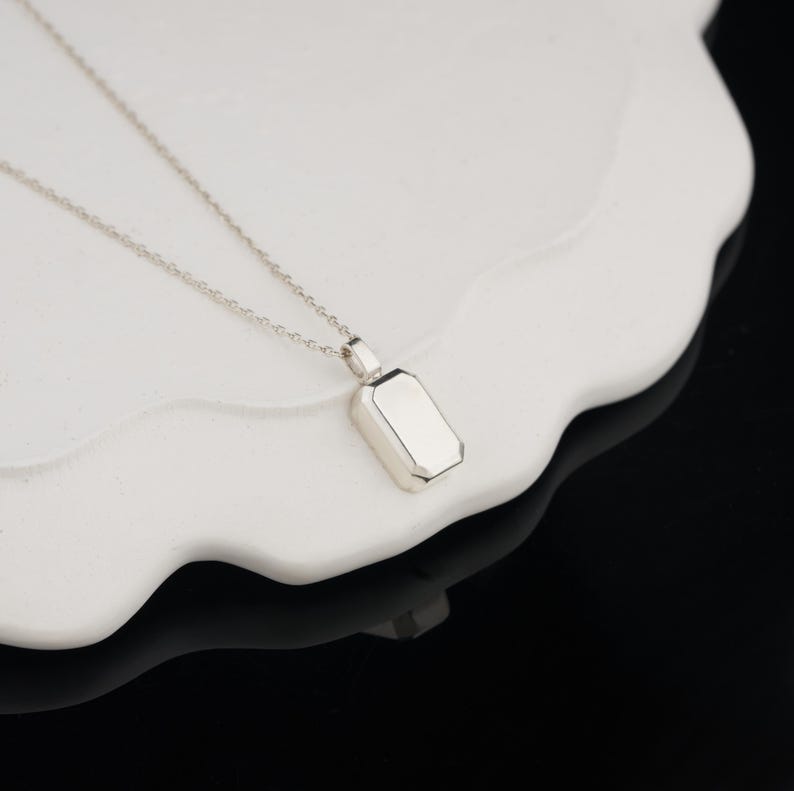Peut inclure: Un collier en argent avec un pendentif rectangulaire. Le pendentif a une surface lisse et polie.