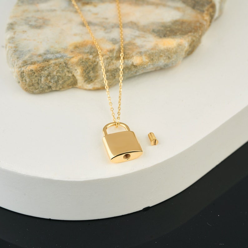 May include: A gold chain necklace with a padlock pendant. The padlock has a small screw on the side.