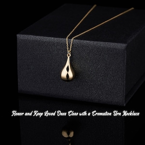 Gold teardrop cremation pendant displayed on black gift box with memorial message