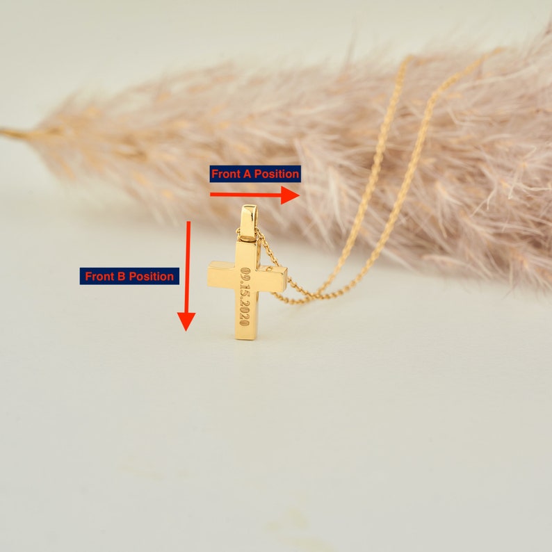 May include: Gold cross necklace with a date engraved on the back. The cross is hanging from a delicate gold chain.