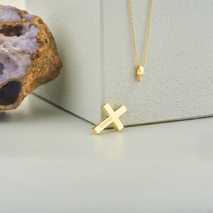 May include: A gold cross pendant necklace with the word "Jessica" engraved on the front. The necklace is on a white surface.