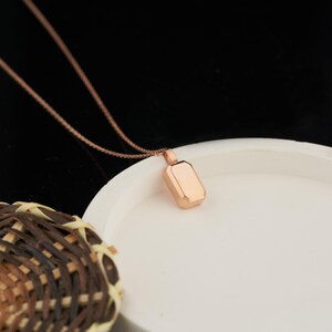 Peut inclure: Un collier en or rose avec un pendentif rectangulaire. Le pendentif a une finition lisse et polie.