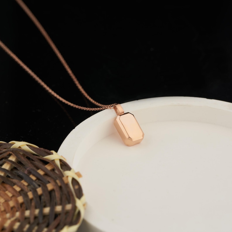 Peut inclure: Un collier en or rose avec un pendentif rectangulaire. Le pendentif a une finition lisse et polie.