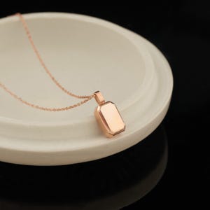 Peut inclure: Un collier en or rose avec un pendentif rectangulaire. Le pendentif a une finition lisse et polie.
