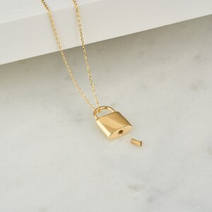 May include: A gold chain necklace with a small gold padlock pendant. The padlock is open and has a small screw on the side.