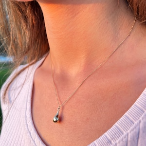 Gold teardrop urn necklace worn outdoors on model’s neck, close-up view