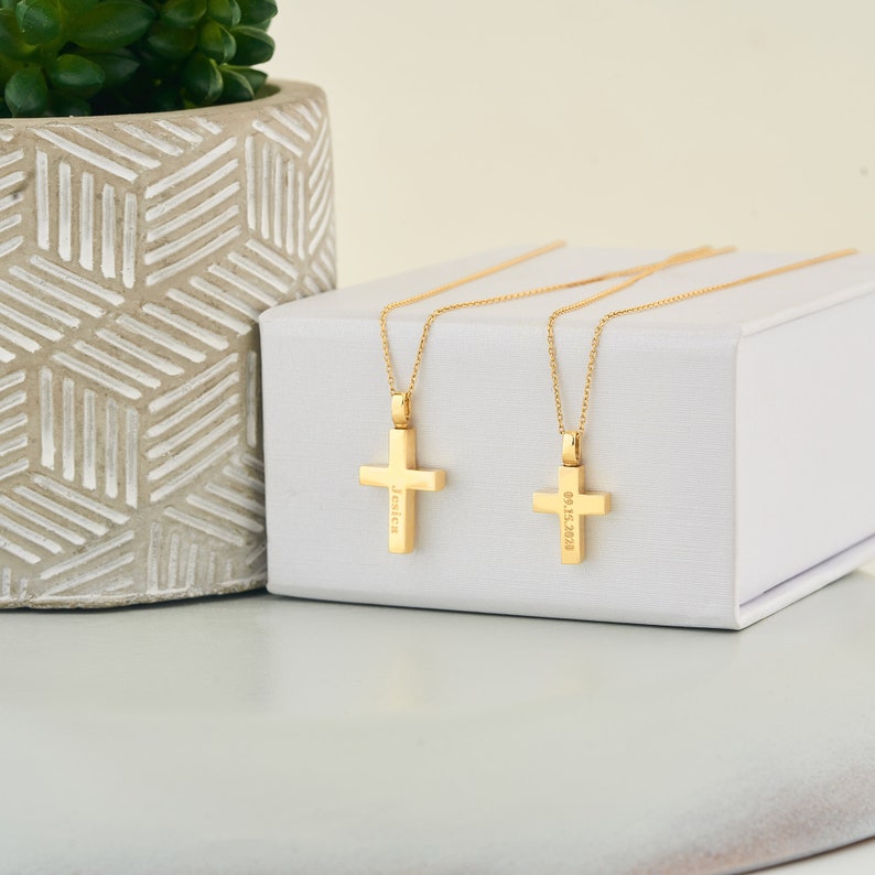 May include: Two gold cross necklaces on a white box. One cross is engraved with the name "Jessica" and the other with the date "03.13.2020".