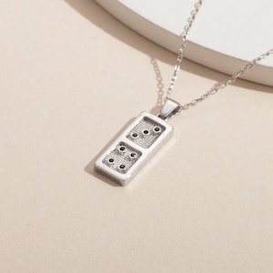 May include: A silver chain necklace with a silver domino pendant. The domino has black dots on a white background.