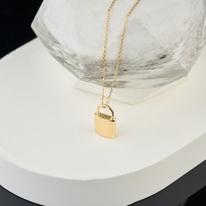 May include: A gold chain necklace with a padlock pendant. The padlock is a simple, solid design.