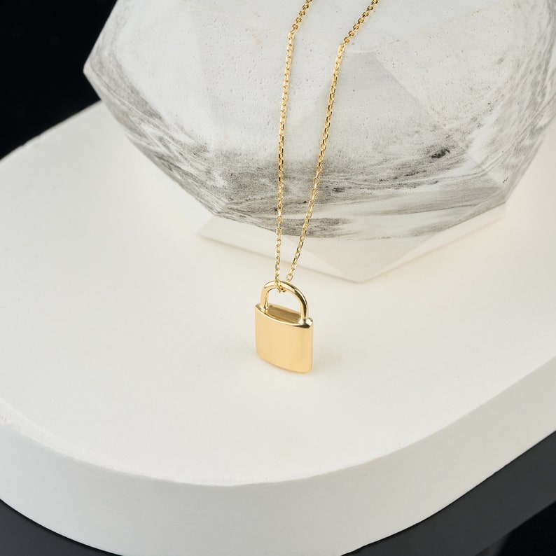 May include: A gold chain necklace with a padlock pendant. The padlock is a simple, solid design.