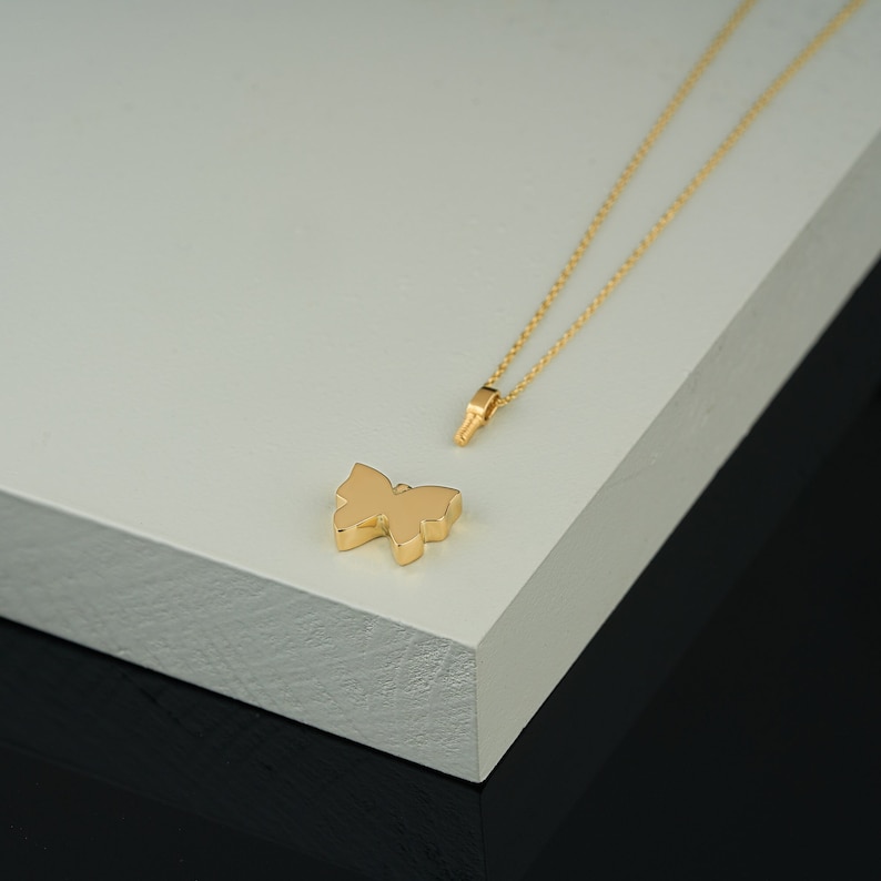 Puede incluir: Un collar de cadena de oro con un colgante de mariposa. El colgante es un dise&ntilde;o simple de oro macizo.