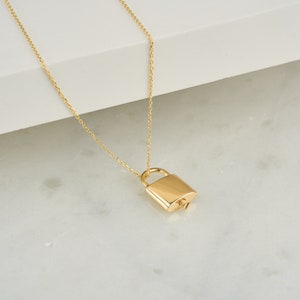 May include: A gold chain necklace with a padlock pendant. The padlock is a simple design with a rounded shape.