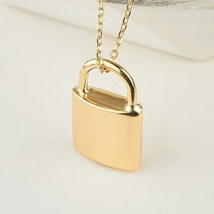 May include: A gold padlock pendant necklace. The padlock is a simple design with a rounded top and a flat bottom. The chain is a delicate, thin chain.