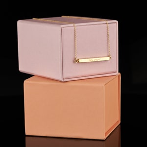 May include: A gold bar necklace with the inscription "My angel" in a pink and peach box.