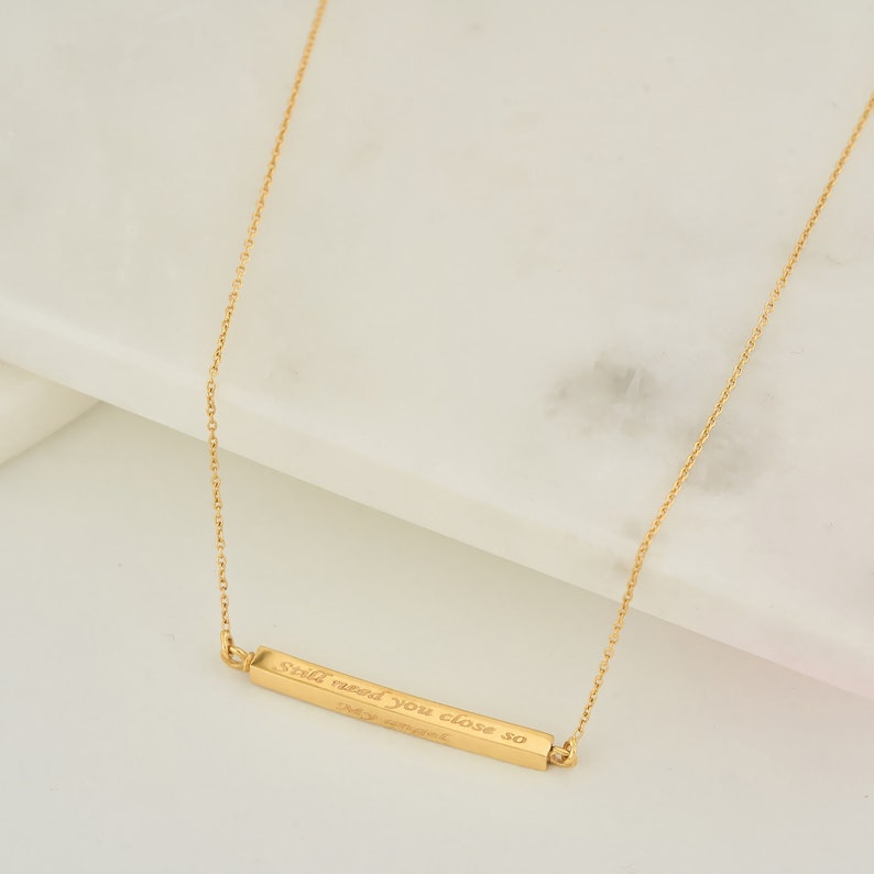 May include: Gold bar necklace with the inscription "Still need you close so I can breathe".