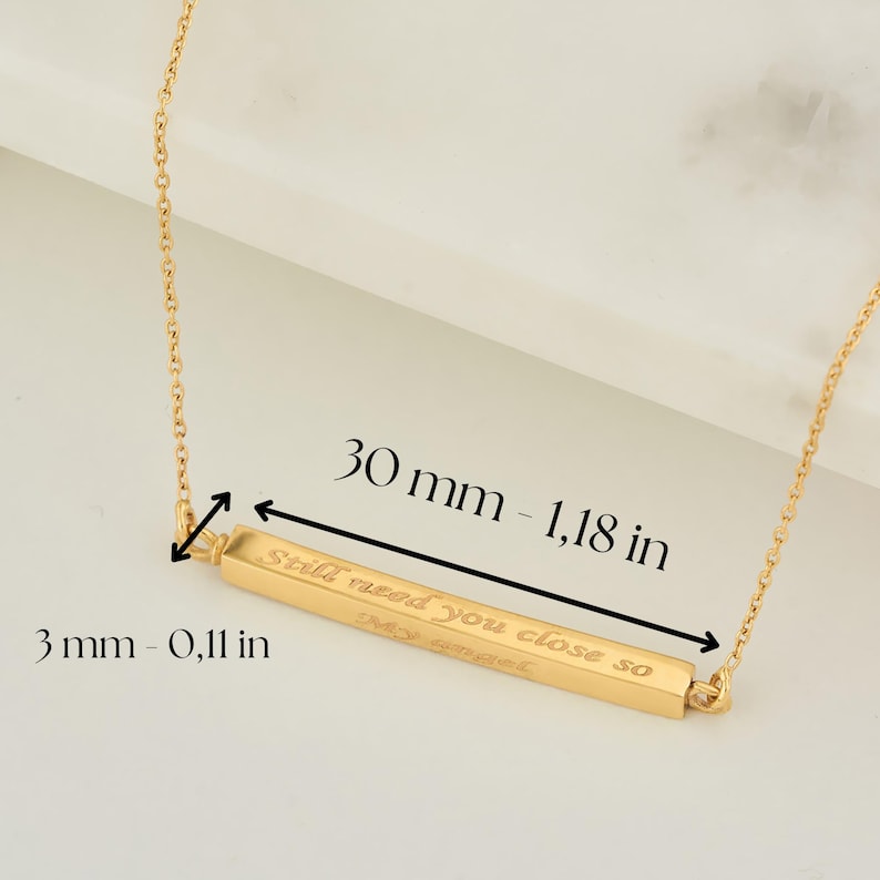 May include: Gold bar necklace with the inscription "Still need you close so". The bar is 1.18 inches long and 0.11 inches wide.