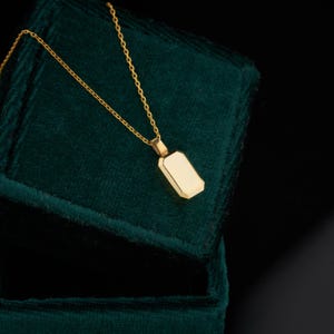 Peut inclure: Un collier en or avec un pendentif rectangulaire, reposant sur un &eacute;crin en velours vert fonc&eacute;.