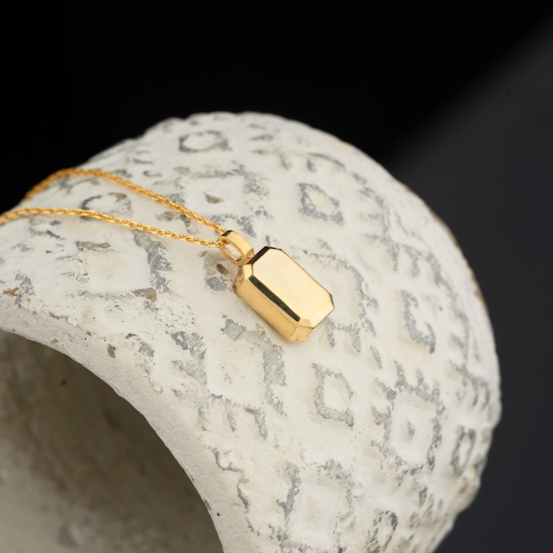 Peut inclure: Un collier en cha&icirc;ne dor&eacute;e avec un petit pendentif rectangulaire. Le pendentif a une surface lisse et polie et est l&eacute;g&egrave;rement inclin&eacute;.
