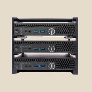 May include: Three black Dell OptiPlex 3060 computers stacked in a black metal rack. Each computer has a Dell logo and multiple ports. The rack is designed to hold the computers securely.