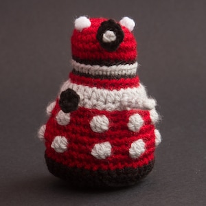 May include: A crocheted red and white toy with black accents. The toy has a round body with white polka dots and a black eye. The toy is made of yarn and has a textured surface.