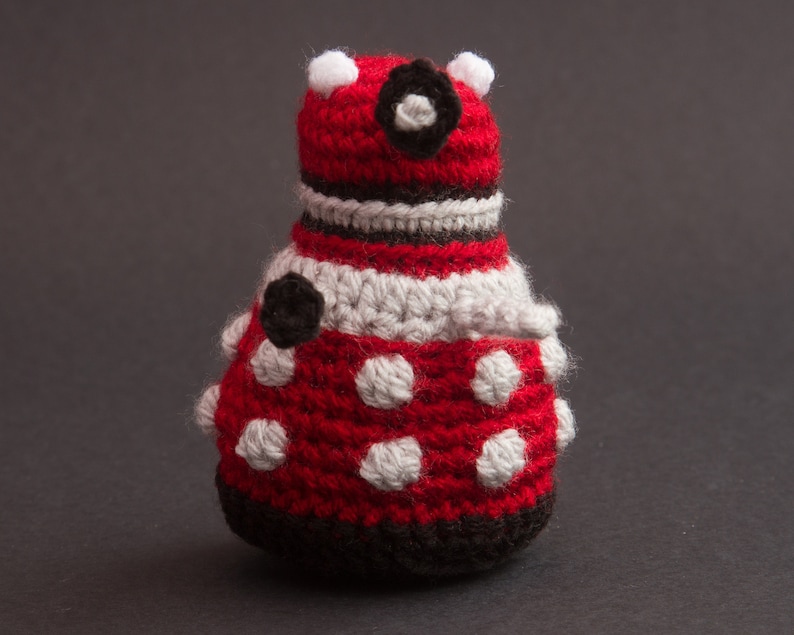 May include: A crocheted red and white toy with black accents. The toy has a round body with white polka dots and a black eye. The toy is made of yarn and has a textured surface.