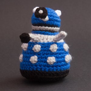 May include: Blue and white crocheted toy robot with a black eye and a white antenna.