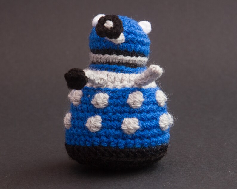 May include: Blue and white crocheted toy robot with a black eye and a white antenna.