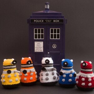 May include: Five crocheted Dalek figures in different colours, standing in front of a blue police box with the text "Police Public Call Box".