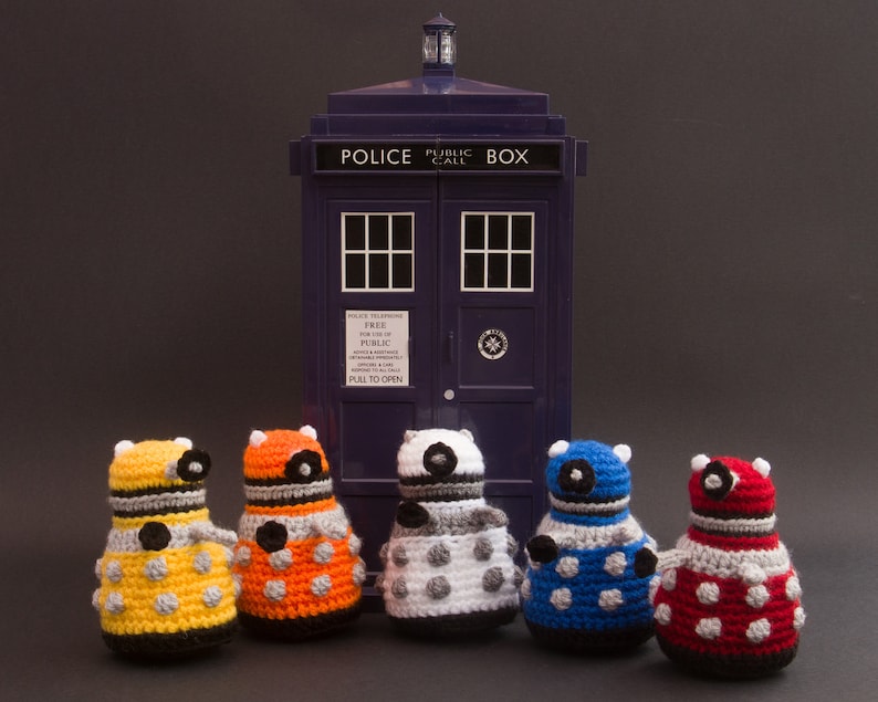 May include: Five crocheted Dalek figures in different colours, standing in front of a blue police box with the text "Police Public Call Box".