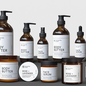 May include: A collection of amber glass bottles and jars with black pump tops and droppers. The labels are white with black text and feature the brand name "The Natura House". The products include body butter, face serum, and a rose and lavender candle.