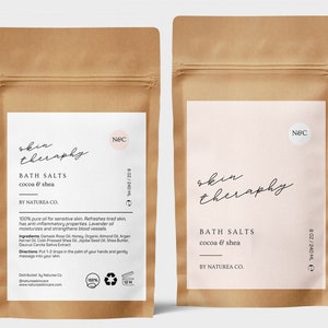 Könnte beinhalten: Zwei braune Papiertüten mit weißen Etiketten. Die Etiketten tragen den Text "skin therapy" in einer handschriftlichen Schriftart. Der Text "Bath Salts cocoa & shea" ist unter dem Logo gedruckt. Der Text "By Naturea Co." ist unter dem Produktnamen gedruckt. Die Beutel sind 8 Unzen oder 240 Milliliter.