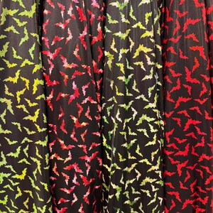 May include: Close-up of black fabric with a repeating pattern of colorful bats. The bats are in shades of green, red, and pink. The fabric is folded, creating vertical lines.