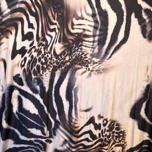 Puede incluir: Tela con un diseño de estampado animal mixto. El patrón combina rayas de cebra y manchas de leopardo en tonos negros, marrones y crema. La tela tiene una apariencia fluida y texturizada.