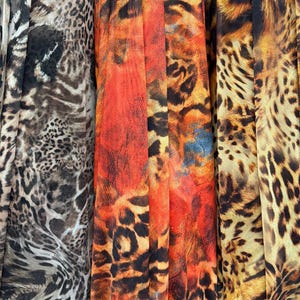 Puede incluir: Primer plano de tres telas diferentes con estampados de animales. Las telas presentan estampados de leopardo y tigre en tonos marrones, naranjas y negros. Las telas están drapeadas, mostrando su textura y diseño.