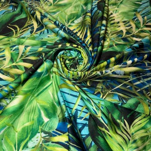 May include: Vibrant fabric with a tropical leaf pattern in shades of green, blue, and yellow. The fabric is folded and draped, showcasing the detailed design of large and small leaves. The color palette creates a lush, jungle-like aesthetic.