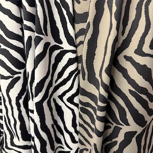 May include: Close-up of two fabrics with zebra stripe patterns. One fabric is black and white, the other is tan and black. The fabric is draped, showing the texture and flow of the material. The zebra print is a classic animal print.