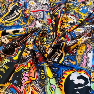 May include: A vibrant fabric with a colorful, abstract design. The pattern features a mix of shapes and illustrations in shades of blue, yellow, pink, orange, and black. The fabric is folded, creating a dynamic display of the artwork.